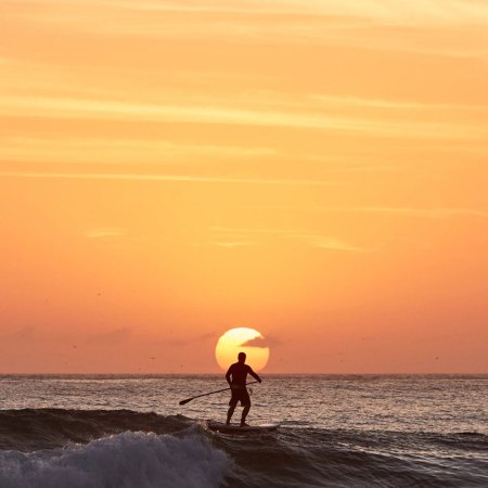 A man on a SUP board against a setting sun.