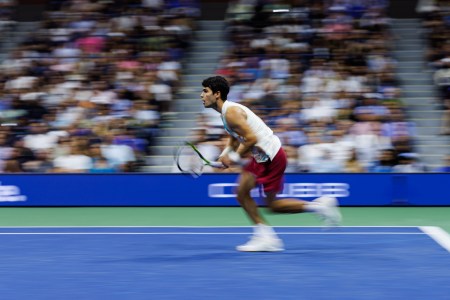 A photo of Carlos Alcaraz running for the tennis ball, with his mouth open.