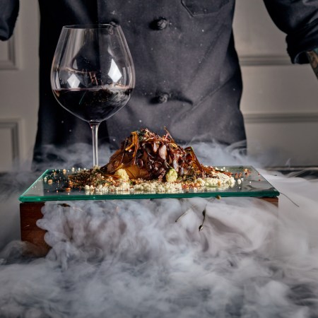 Surf and turf next to a glass of wine surrounded in smoke