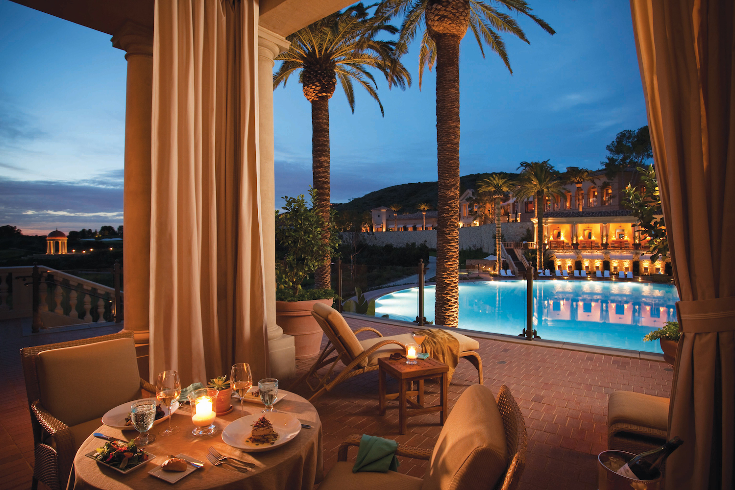 Dining table under a cabana next to a pool at nighttime
