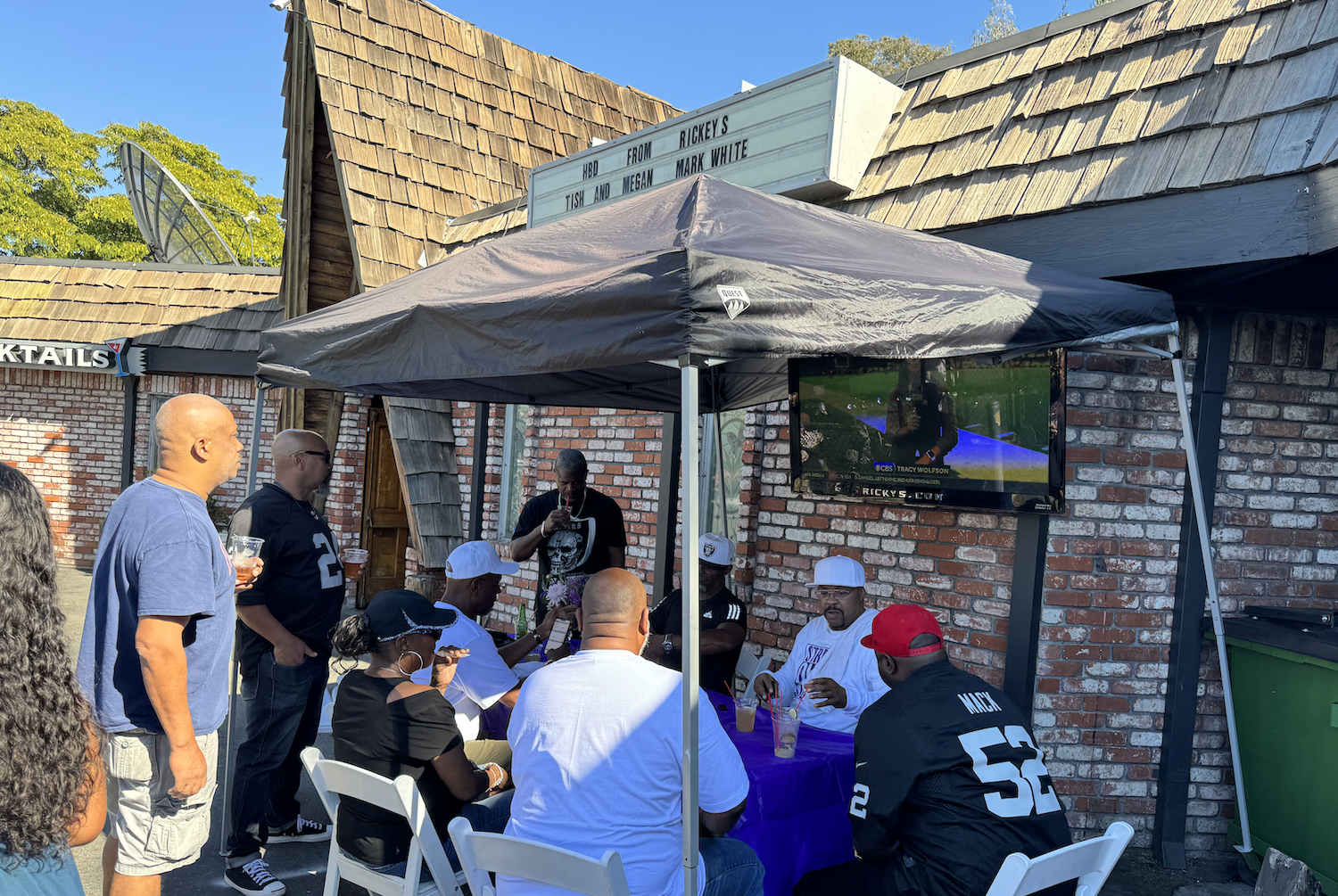 People sitting under a canopy outside watching TV