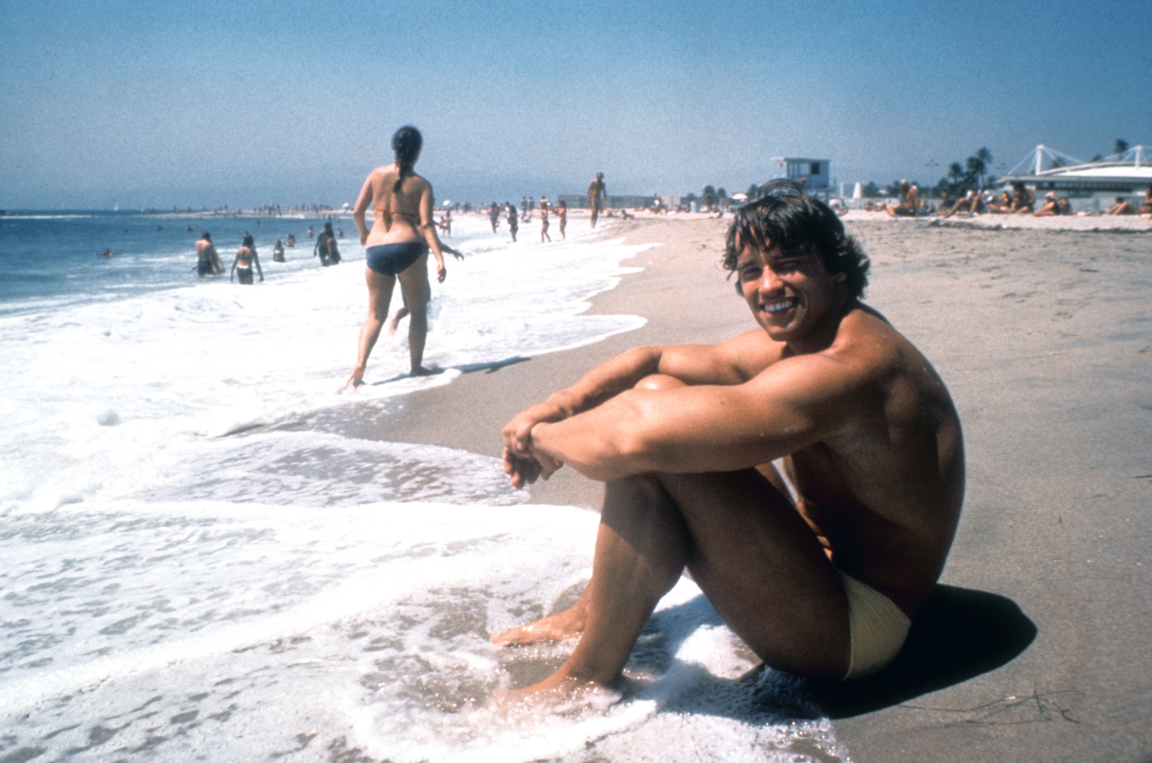 Arnold Schwarzenegger sitting on the beach, in his 20s, grinning. We look at the life lessons in his new book, "Be Useful"