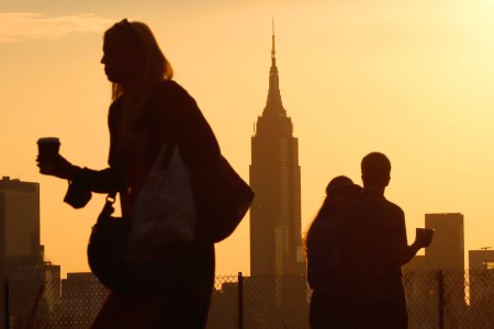 Morning commuters walk with coffees at sunrise, the Empire State Building in the background.