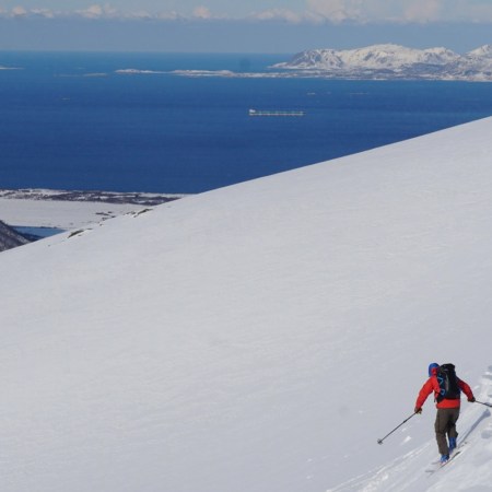 A skier on an empty mountain with the ocean in the background.