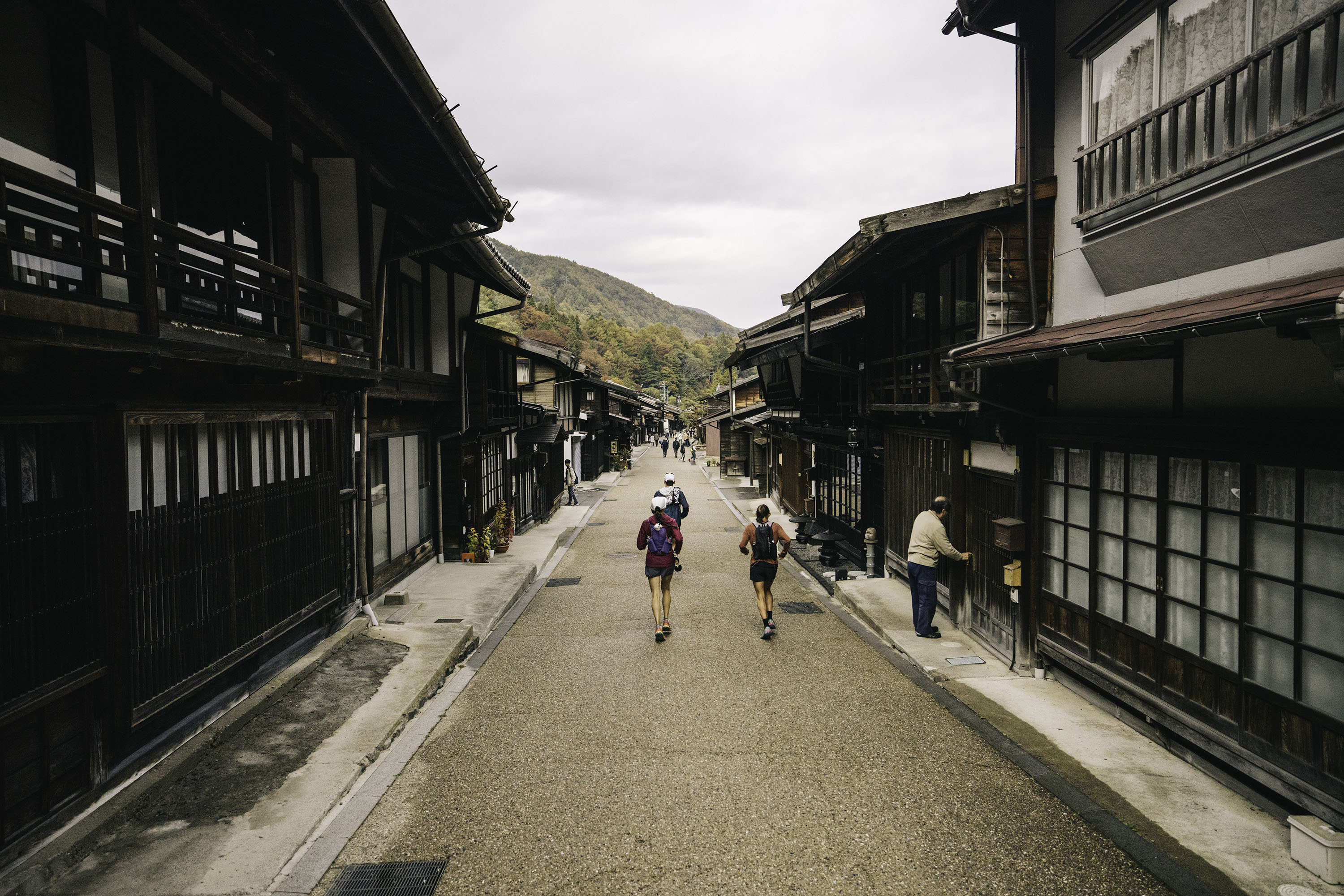 Runners on a quiet road in the Japanese Alps, running past shop keepers.