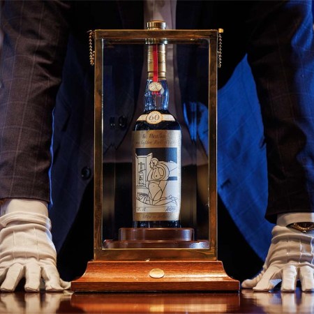 A man (neck down) standing over a bottle of The Macallan Adami 1926, which just broke a spirits auction record