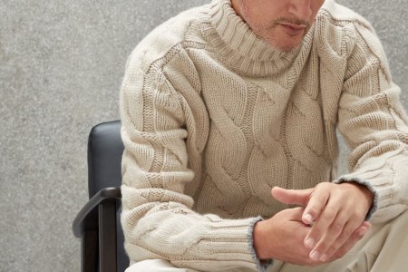 a model in a chunky turtleneck in a chair on a grey background
