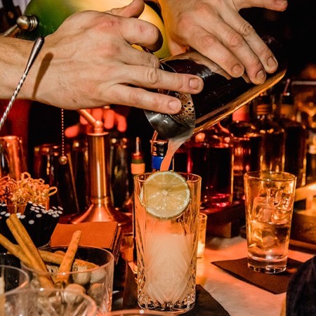 Close-up of hands pouring a cocktail into a glass