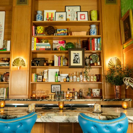 Marble bar with bright blue chairs and shelves with art and bottles of various spirits