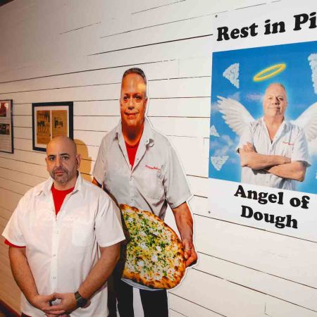 Matthew Katakis stands next to a lifesize photo of his former chef and business parter at his Astoria pizzeria