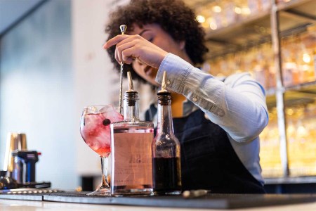 A woman preparing cocktails behind a bar, front view. Bacardi's latest Cocktail Trends Report suggests what we'll be consuming in 2024.