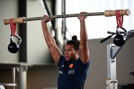 A man in a gym lifting a barbell with a kettlebell attached. This is what's known as chaos training.