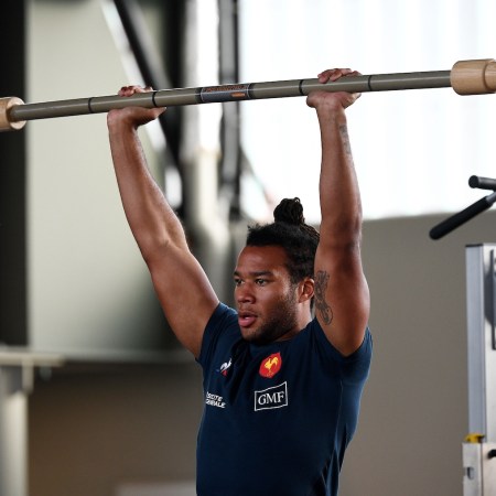 A man in a gym lifting a barbell with a kettlebell attached. This is what's known as chaos training.