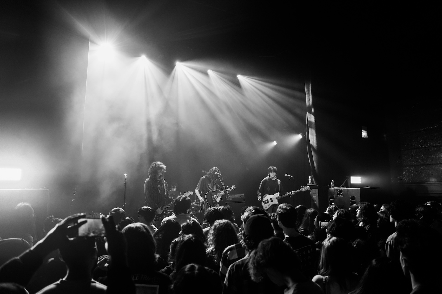Band playing on a stage in front of a large crowd in black & white