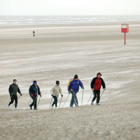A group of adults Nordic walking across a cold beach.