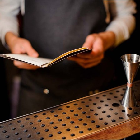 Bartender standing on the bar counter with a recipe book ready to preparing an alcoholic summer cocktail