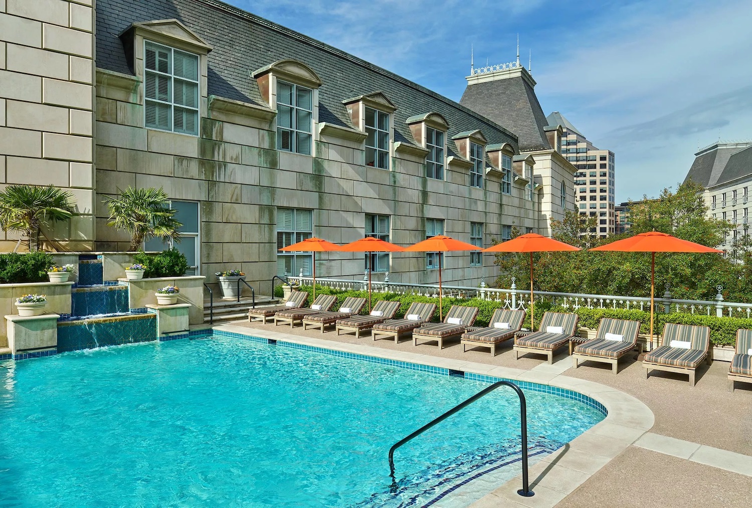 Pool on terrace with greenery, chairs, umbrellas and a waterfall attachment in the pool