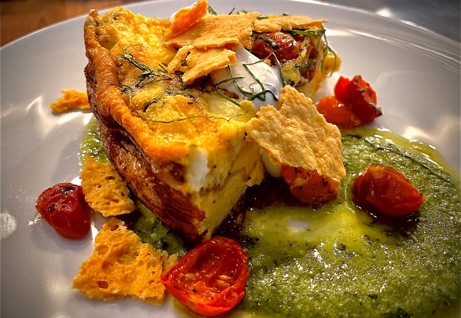 Large slice of frittata with tomatoes and green sauce