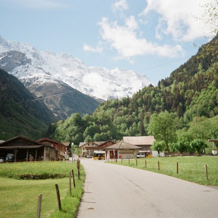 A road cuts through a scenic mountain valley with small Swiss huts not far away.