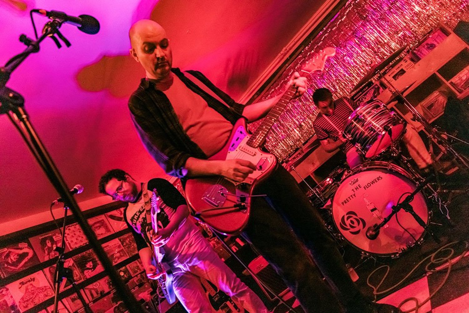 Shot of person playing guitar on a stage with a guitarist and drummer in the background