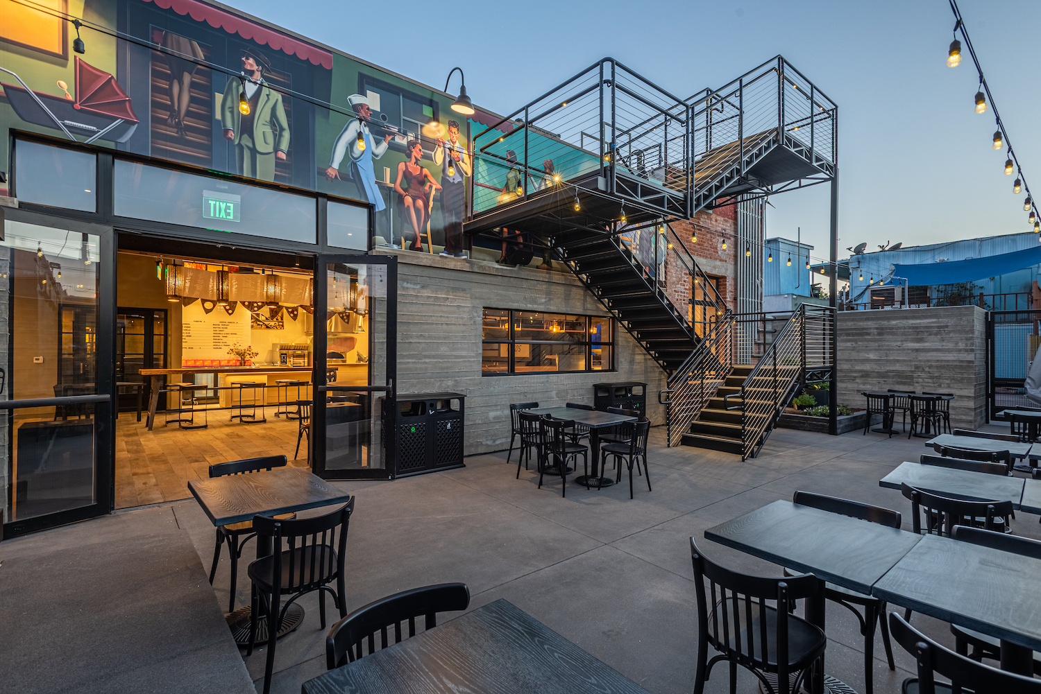 Outdoor terrace with tables, chairs, a mural and steps going to roof