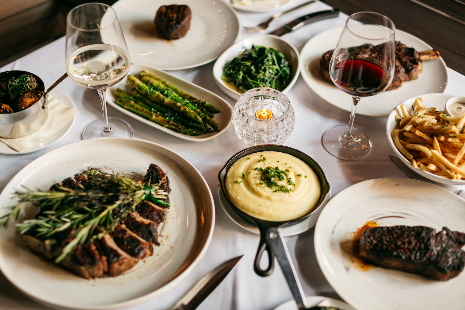 Steak on a plate with wine glasses, broccoli, asparagus and mashed potatoes