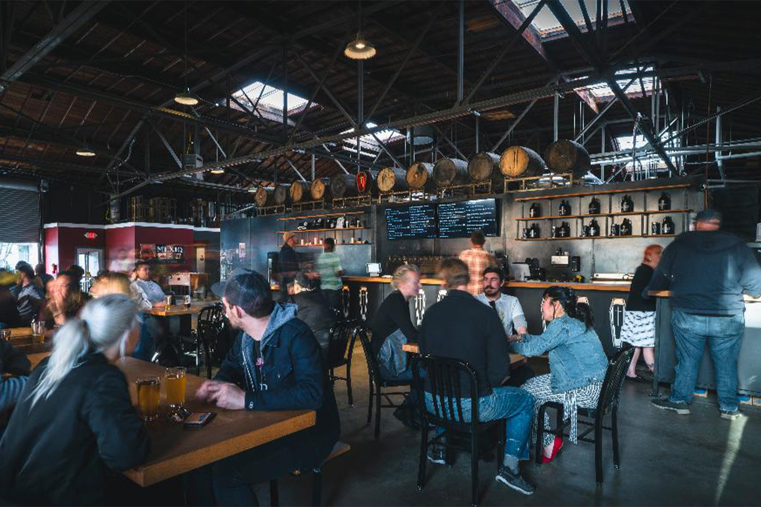 People sitting at tables in a taproom with large barrels