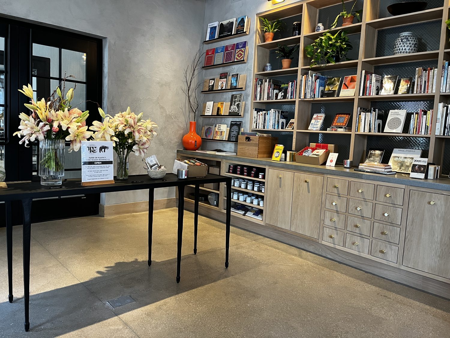 books and plants on shelves, vases with flowers on table