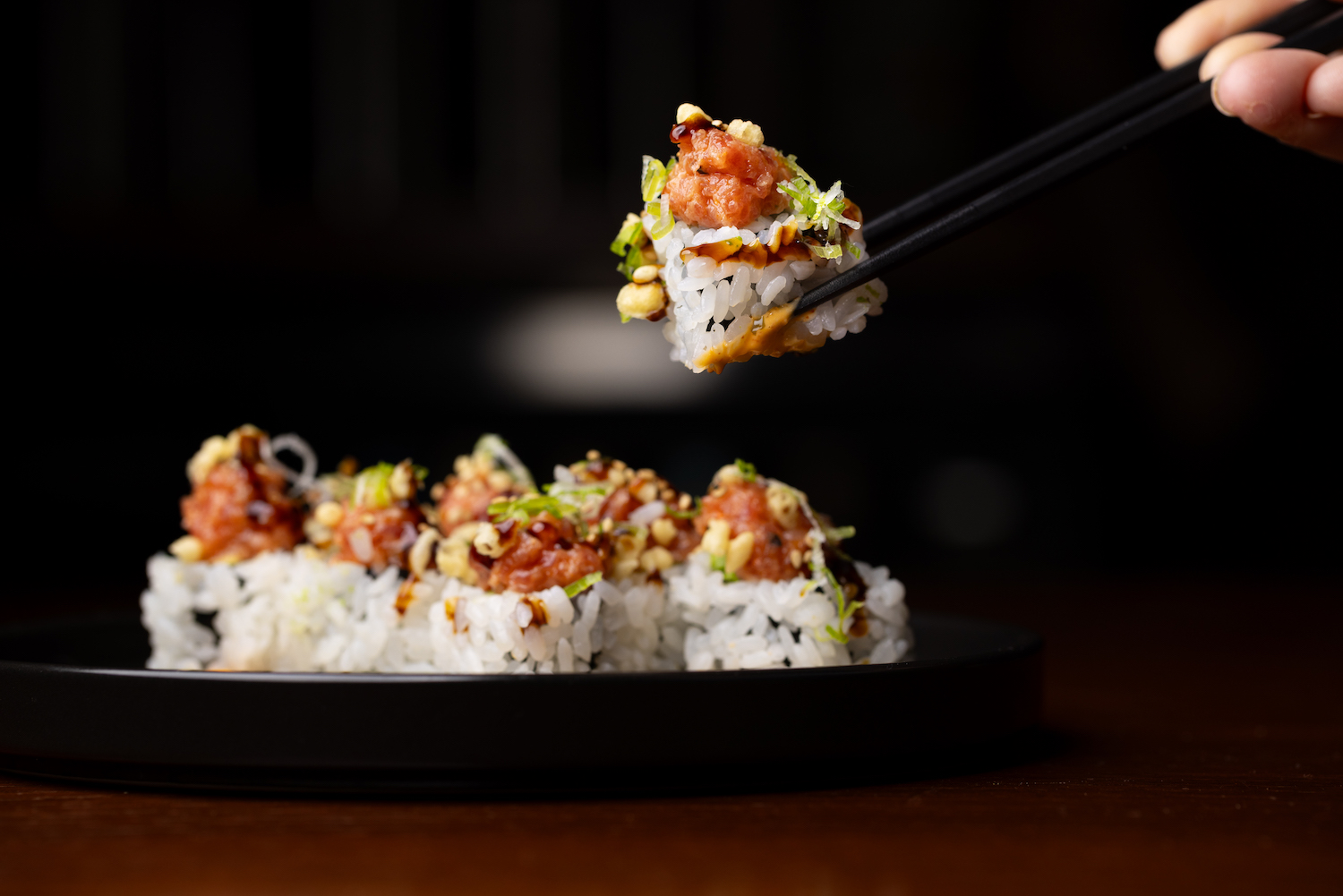 Sushi on a plate being picked up by chopsticks