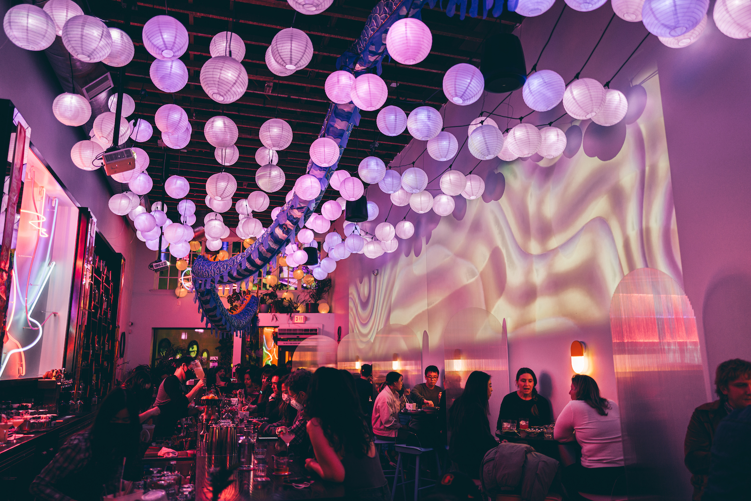 Interior of Viridian with people sitting at bars and high tops, dim-lighting with purple and pink accents light the room