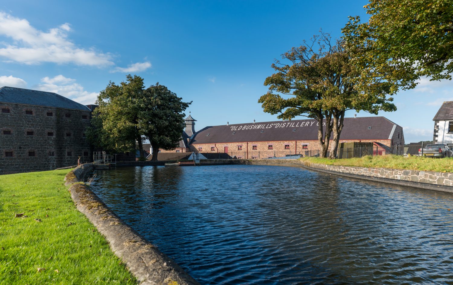 body of water, grass, and trees in front of distillery