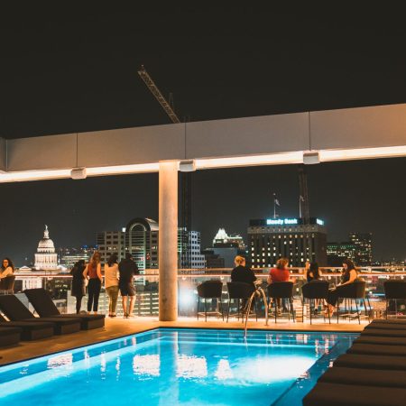 pool on a rooftop at night with people looking over the ledge at skyline