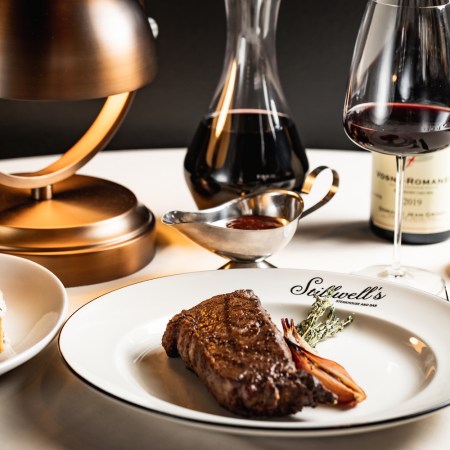 Steak on a plate with gravy and wine on a white tablecloth