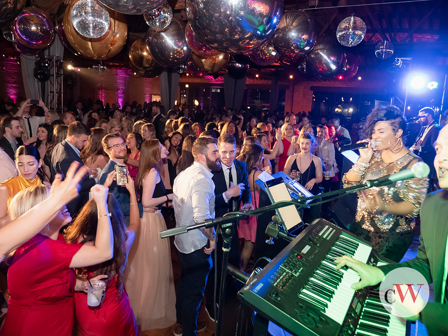 People dancing in a crowd in front of a stage with singers and band members. There are strobe and disco lights across the room.