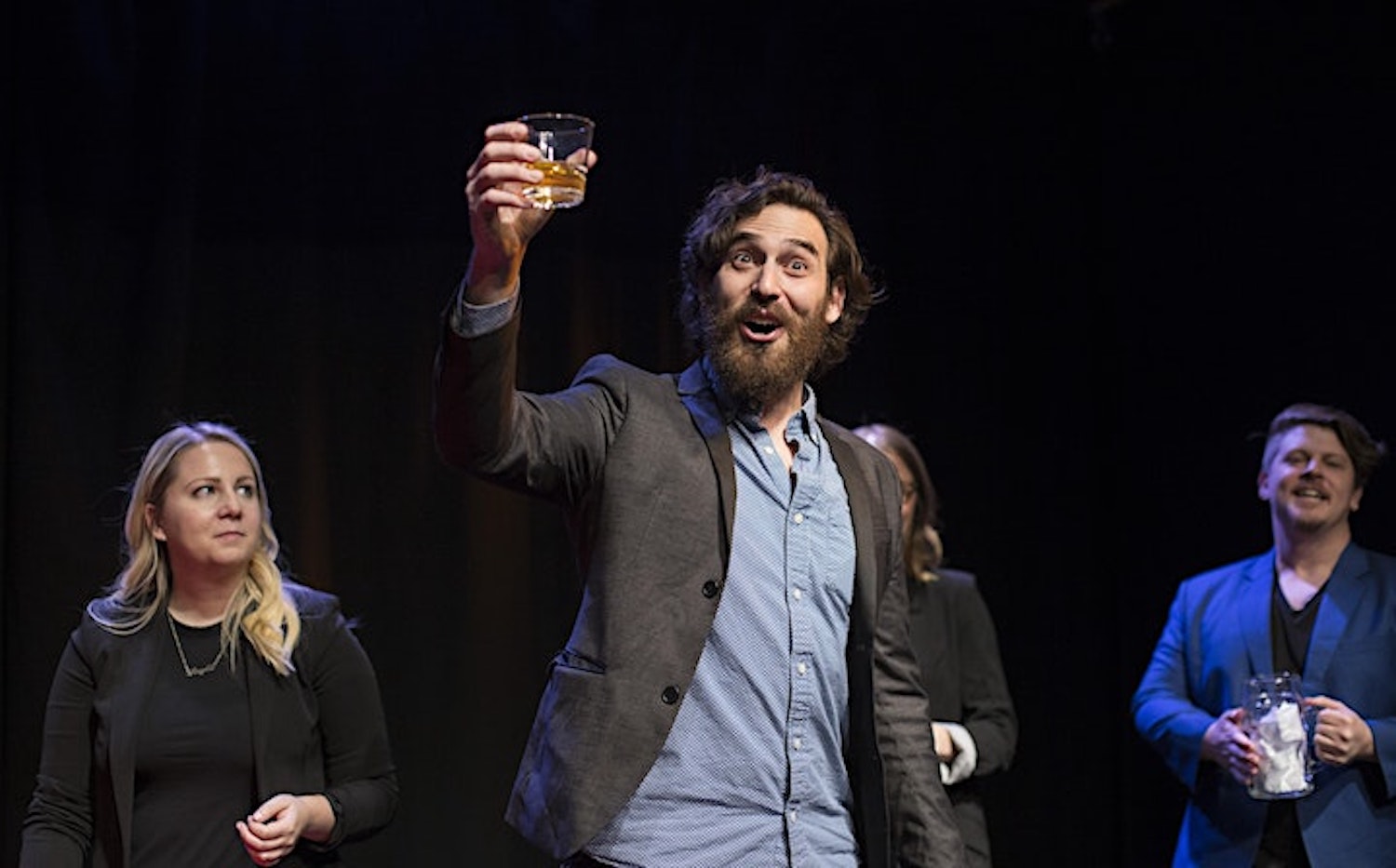 Man on a stage raising a glass in the air in front of a group of people