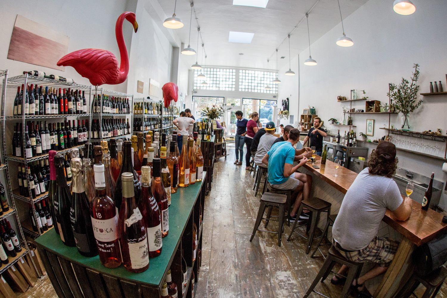 people sitting at bar, liquor on shelves, flamingo statues
