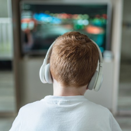 A young boy wearing headphones staring at a TV screen.
