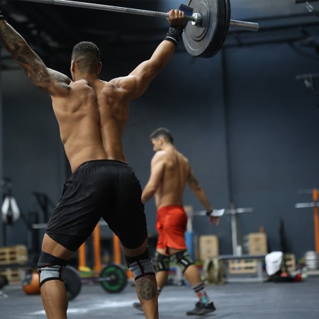 A muscular man lifting a barbell over his head. Here's how strength training can actually give you youthful skin.