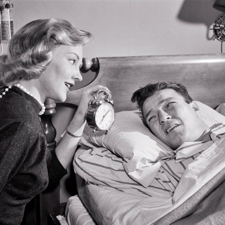 A woman wags an alarm clock in a man's face, urging him to get out of bed. Is sleep divorce right for you? We found a better solution.