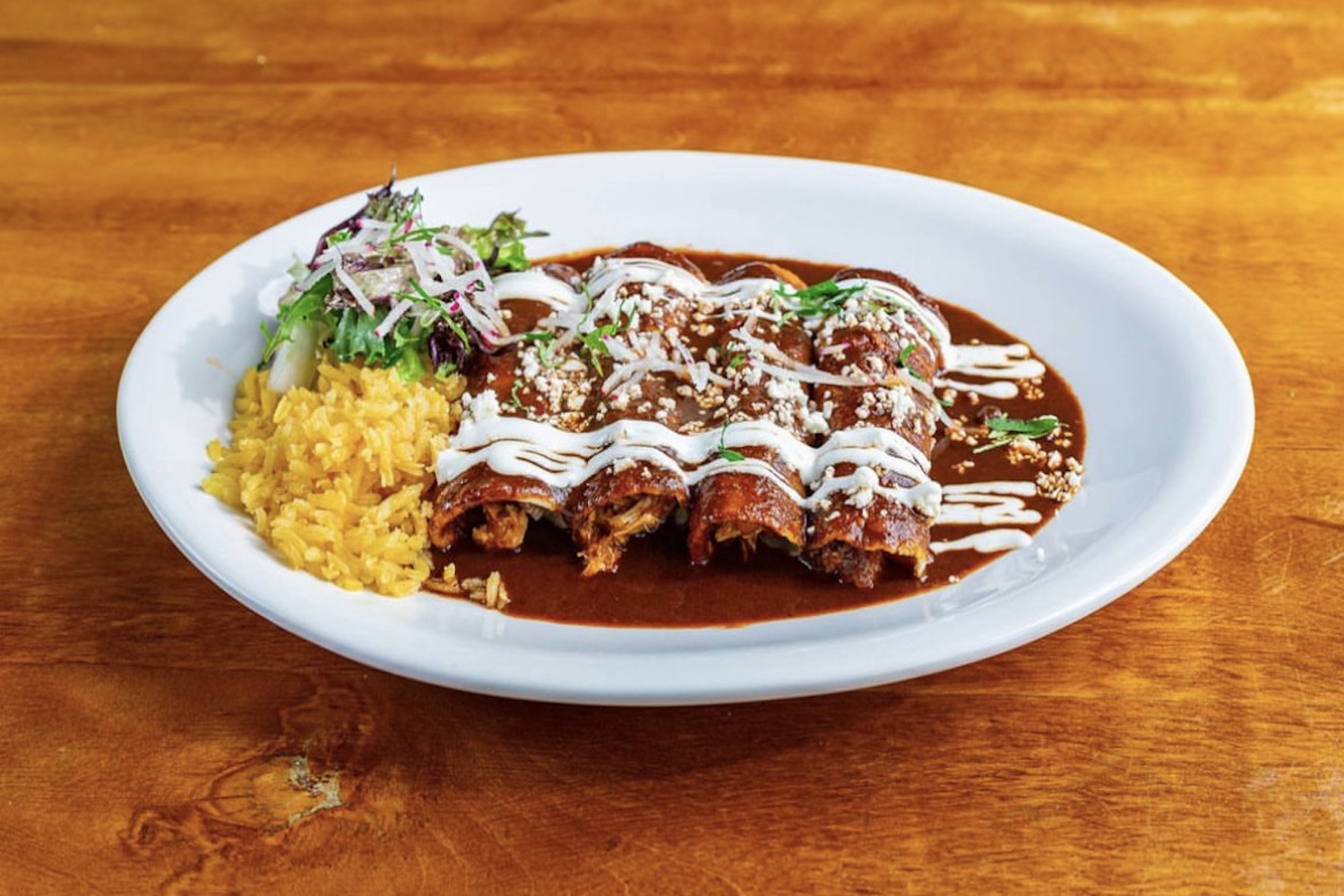 four flautas covered in sauce, yellow rice
