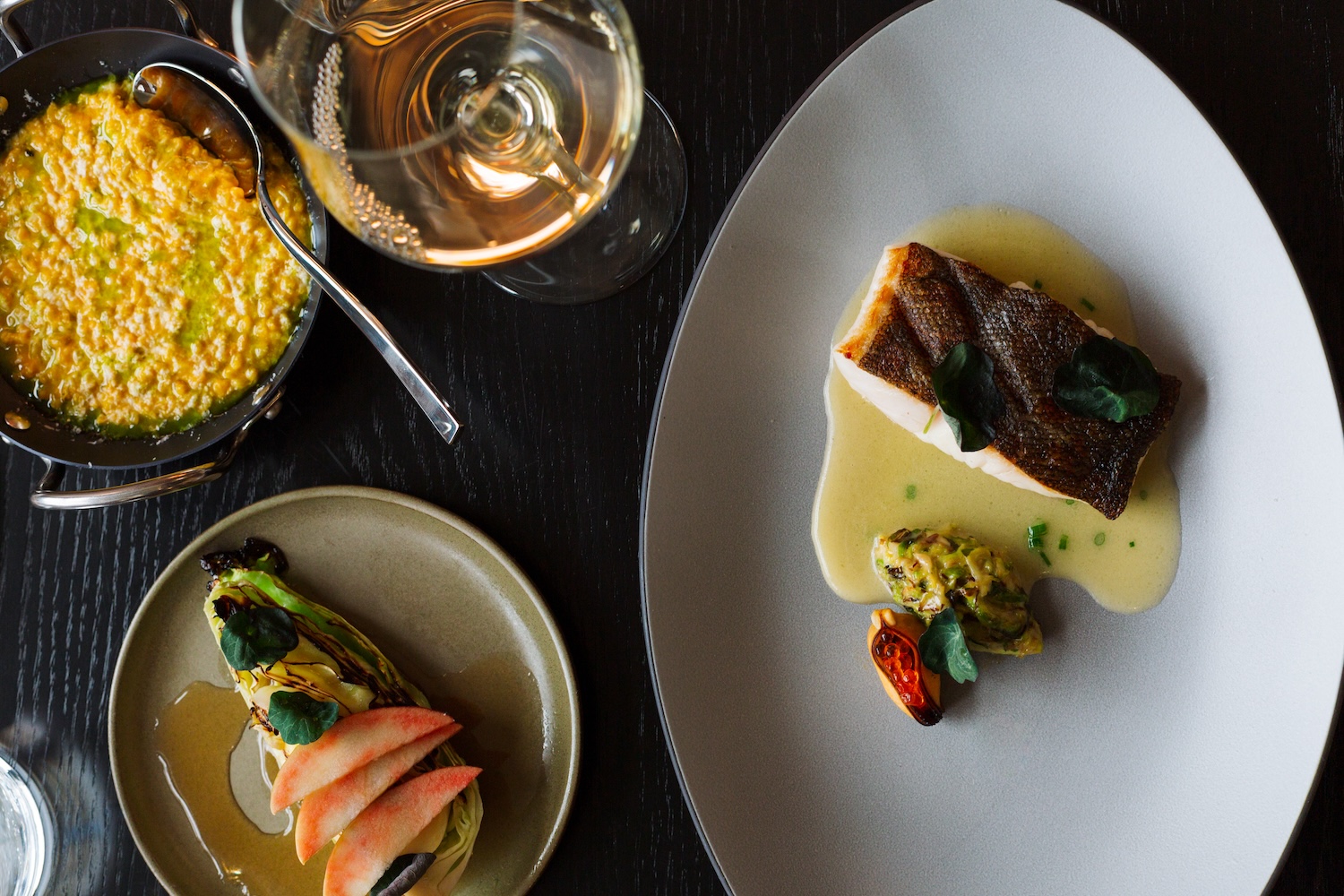 salmon on a plate with yellow sauce, two side plates, glass of wine