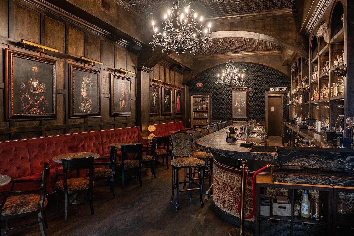 bar with chandeliers, red suede booth, chairs, tables, photos of women hanging,