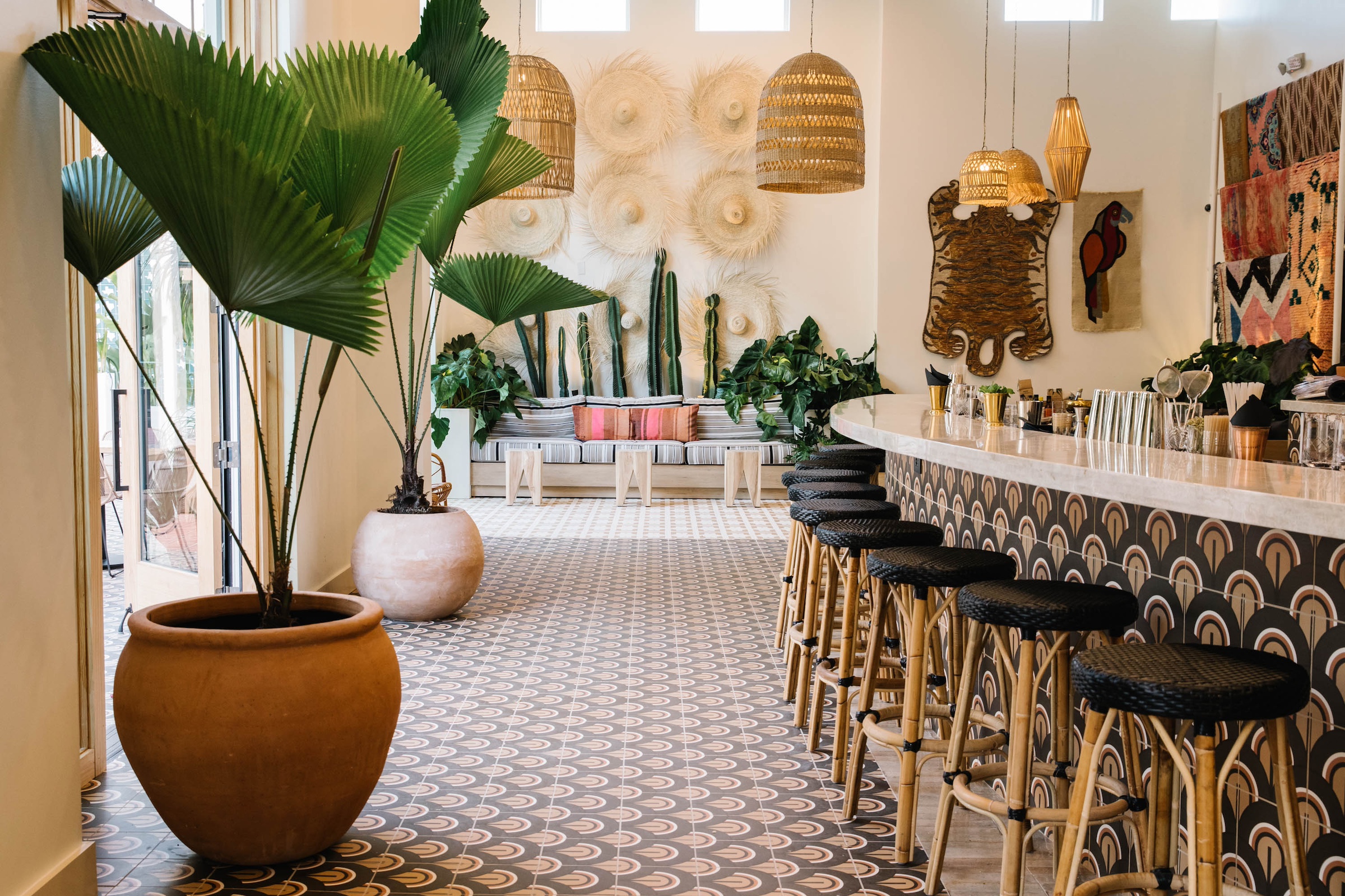 bar with black stools, plants, cacti, straw hats and animal hide hanging on wall, couch with pink pillows