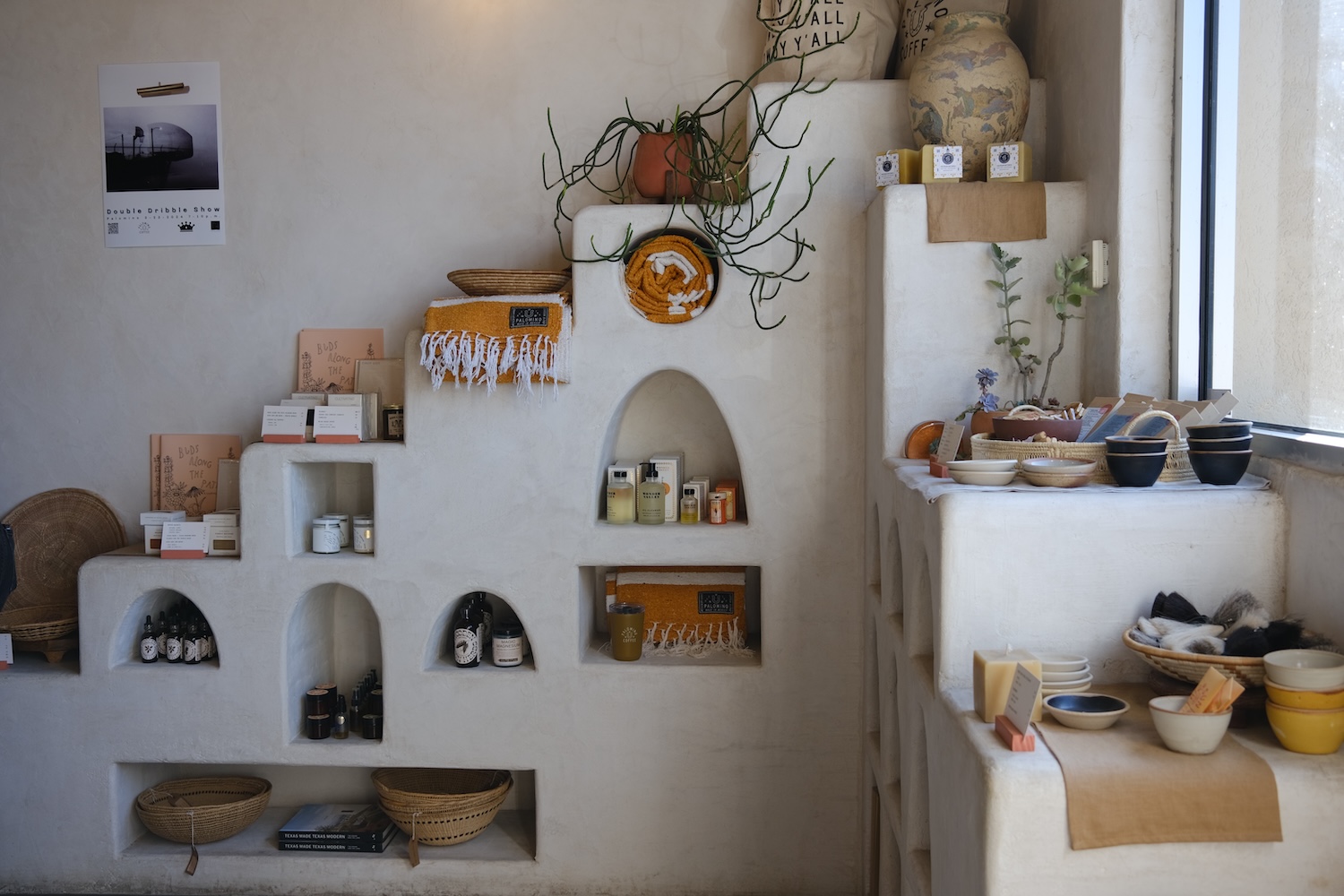 white shelves with towels, oils, bins, ceramics, plant, poster on wall