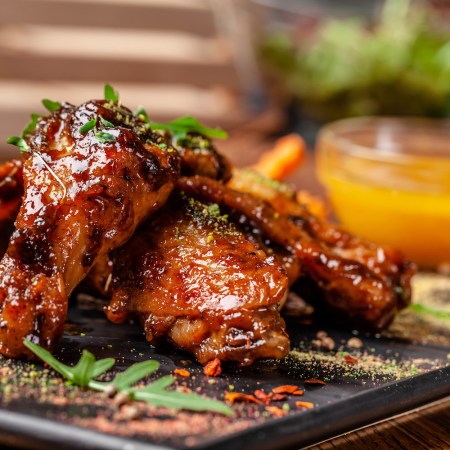 Baked chicken wings and legs in honey mustard sauce. Serving dishes in the restaurant on a black plate
