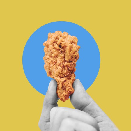 Hand holding fries chicken drumstick, on blue yellow background