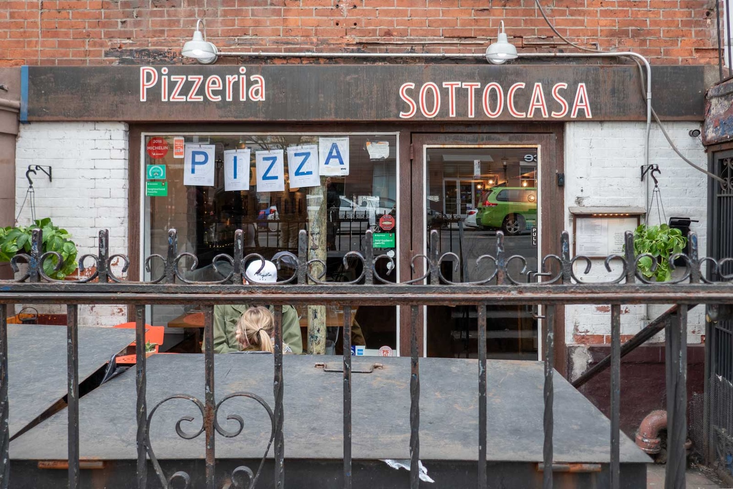 outside of restaurant front, sign that says pizza hanging on window, fence,