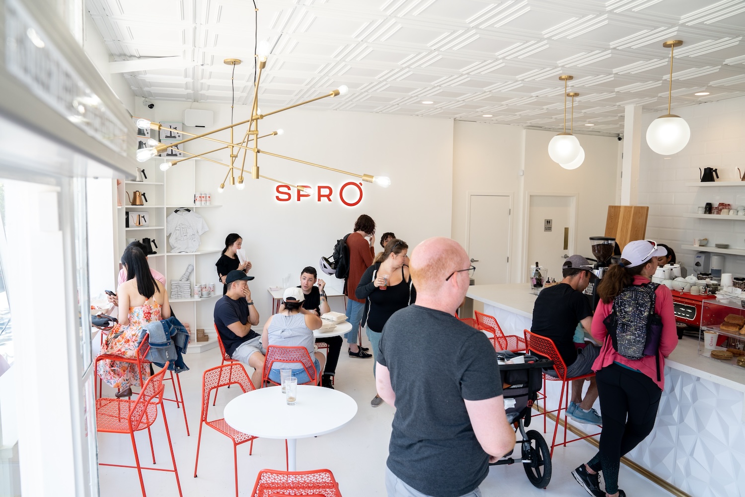 red chairs, white tables, white walls, people standing, gold light hanging