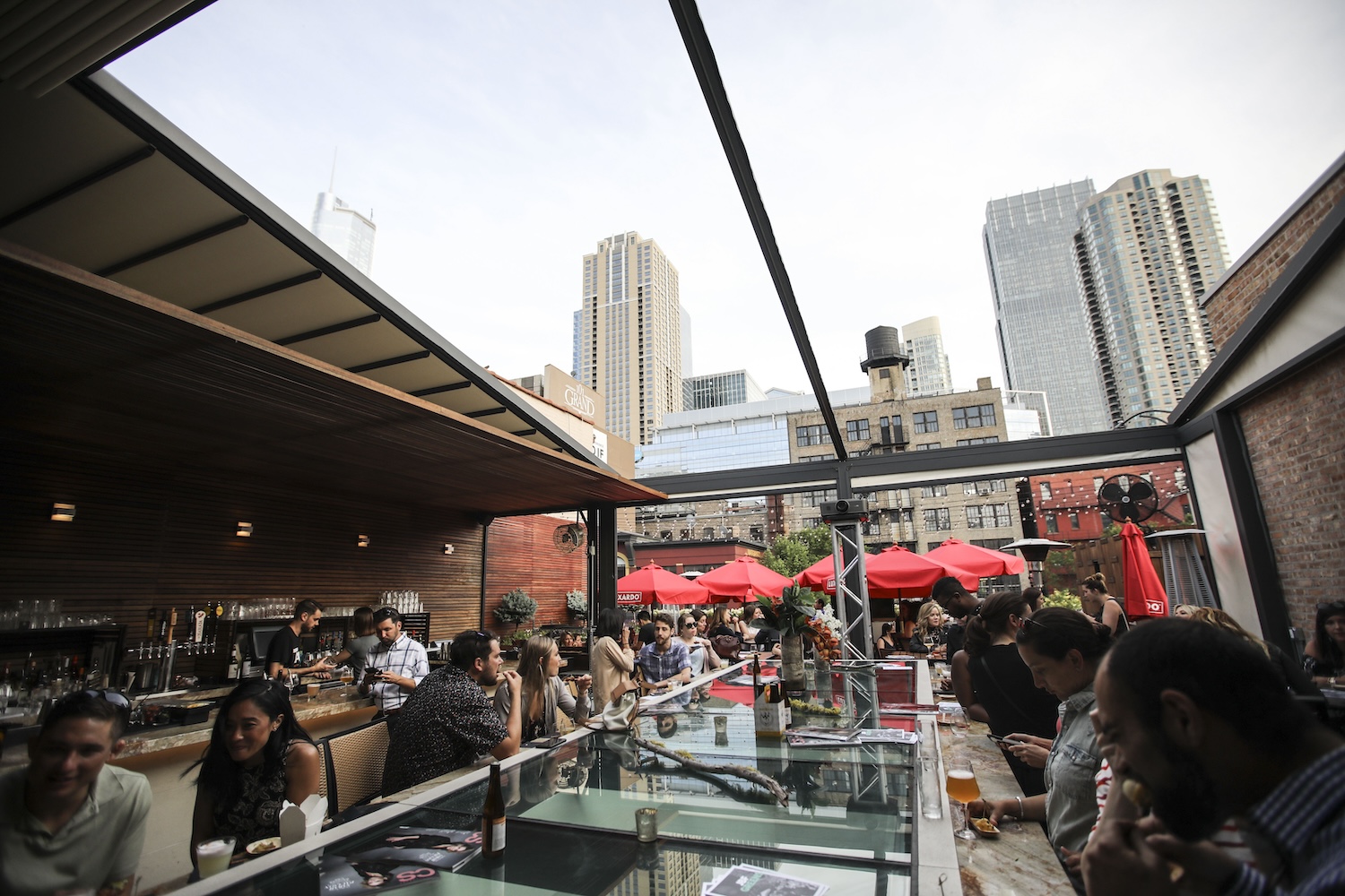 rooftop bar, red umbrellas, fairy lights. glass table, buildings in background