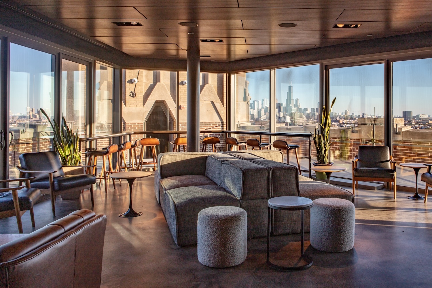 gray couches, gray stools. black chairs, wooden stools, window looking out at city